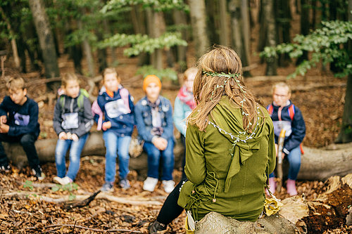 Eine Gruppe von Kindern im Hintergrund, im Vordergrund eine Frau in einem Waldelfenkostüm