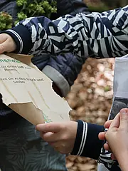 Bild - Eine Hand hält ein zerknittertes Papier mit der Aufschrift: „Alte Buchenwälder schenken Dir deine Luft zum Atmen. Sie halten sie zu dem frisch und sauber.“ Im Hintergrund sind weitere Hände zu sehen, die das Papier betrachten.